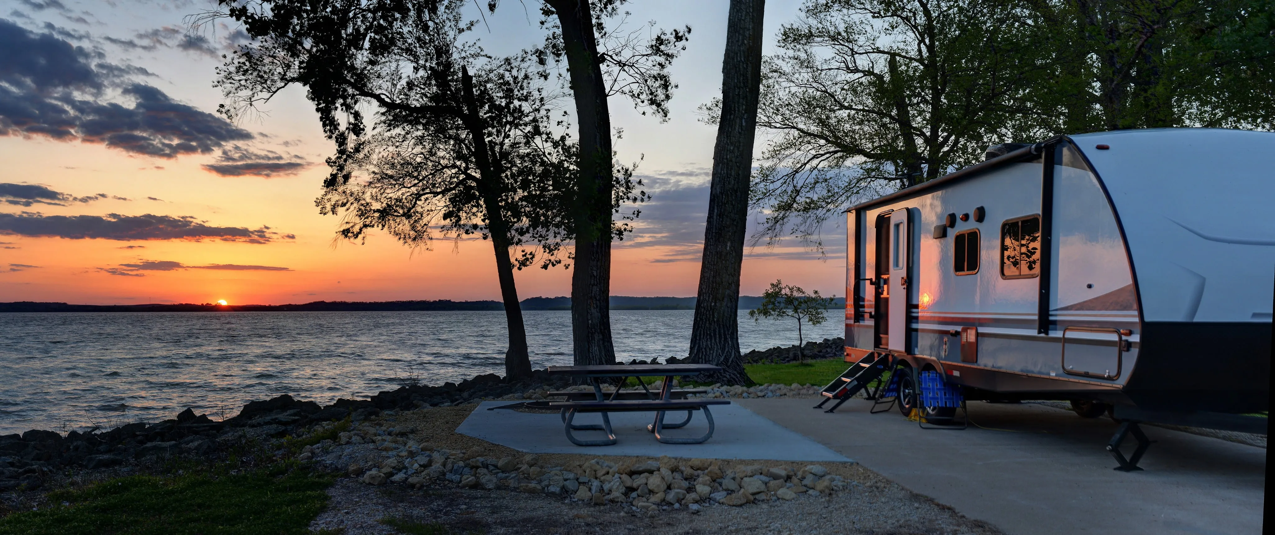 a RV trailer packed and setup in a camp site looking out to a sunset over a lake