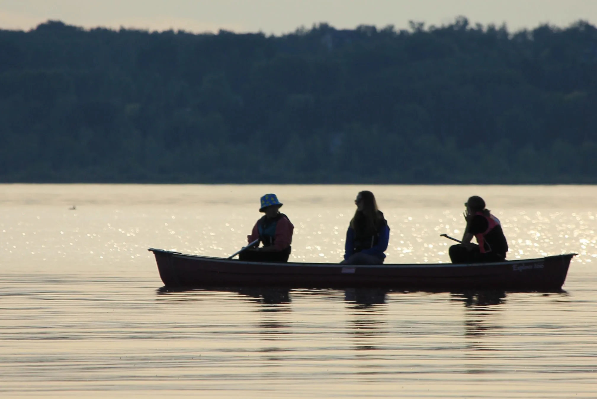 a group of 3 people in a canoe on the lake as sunset